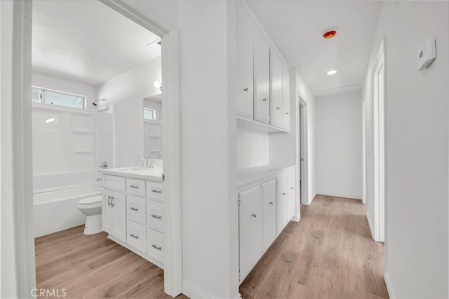 hall featuring light wood-type flooring, a sink, and baseboards