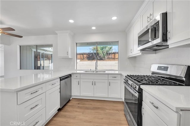 kitchen with light wood finished floors, light countertops, appliances with stainless steel finishes, white cabinetry, and a sink