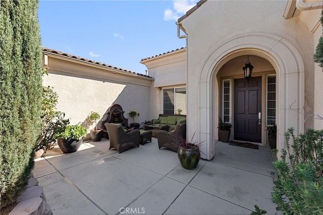 entrance to property featuring a tiled roof, an outdoor living space, a patio, and stucco siding