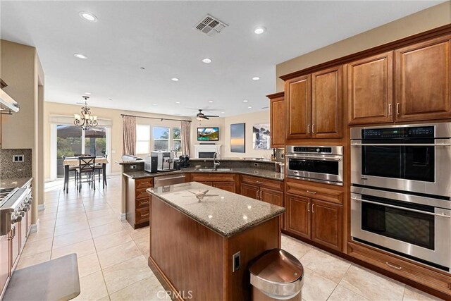 kitchen featuring a peninsula, stainless steel appliances, visible vents, a center island, and brown cabinetry