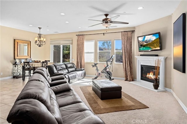 living room featuring ceiling fan with notable chandelier, a glass covered fireplace, baseboards, and recessed lighting