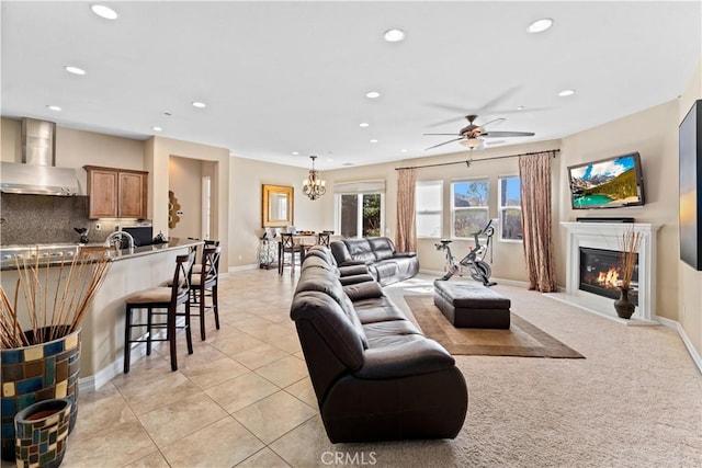 living area featuring light tile patterned floors, baseboards, a glass covered fireplace, ceiling fan with notable chandelier, and recessed lighting