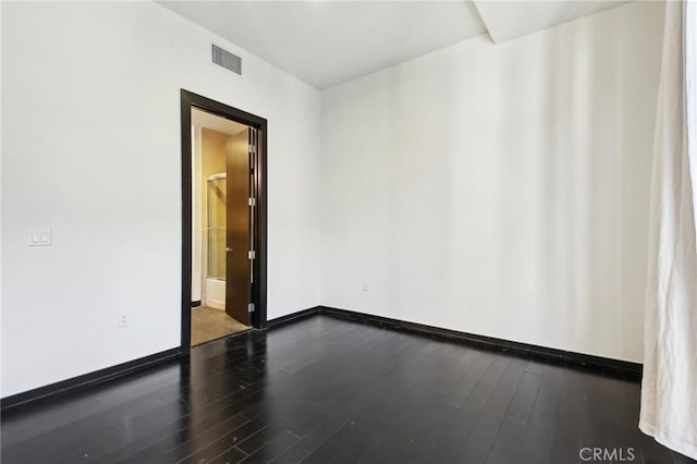 empty room featuring baseboards, dark wood-style floors, and visible vents