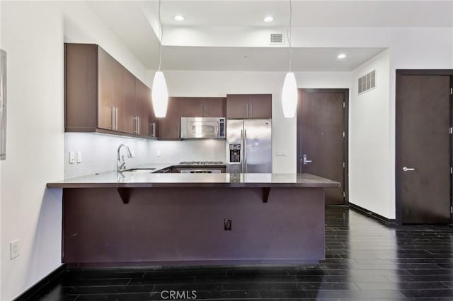 kitchen with a peninsula, dark wood-type flooring, visible vents, appliances with stainless steel finishes, and backsplash