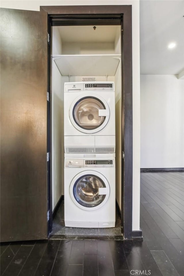 laundry room with stacked washer and dryer, laundry area, dark wood finished floors, and baseboards