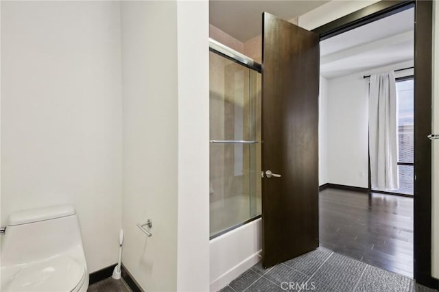 full bathroom with shower / bath combination with glass door, wood finished floors, toilet, and baseboards