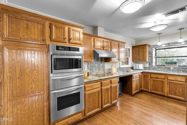 kitchen featuring double oven, under cabinet range hood, visible vents, brown cabinetry, and decorative light fixtures