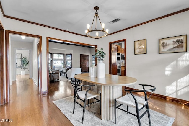 dining area with visible vents, baseboards, light wood-style floors, an inviting chandelier, and crown molding