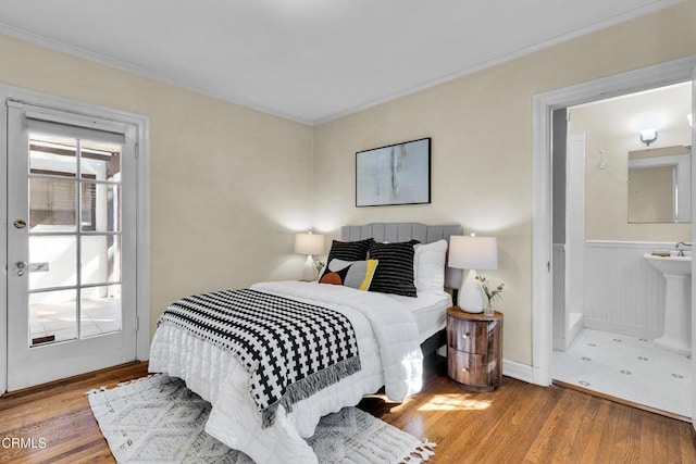 bedroom with crown molding, wainscoting, a sink, and light wood-style floors