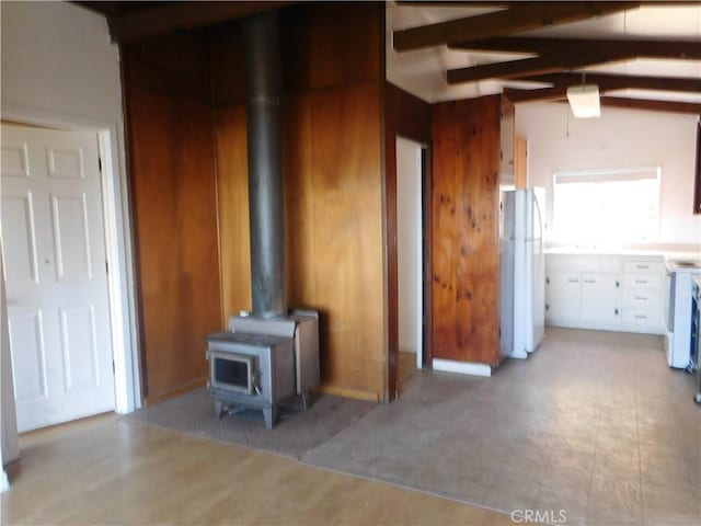 unfurnished living room featuring a wood stove, wood walls, and vaulted ceiling with beams