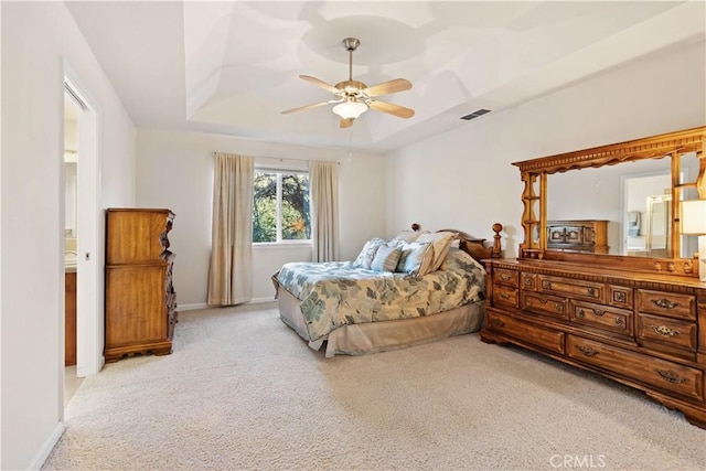 bedroom with light carpet, visible vents, baseboards, a ceiling fan, and a tray ceiling