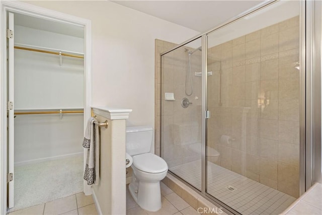 bathroom featuring a spacious closet, tile patterned flooring, toilet, and a shower stall