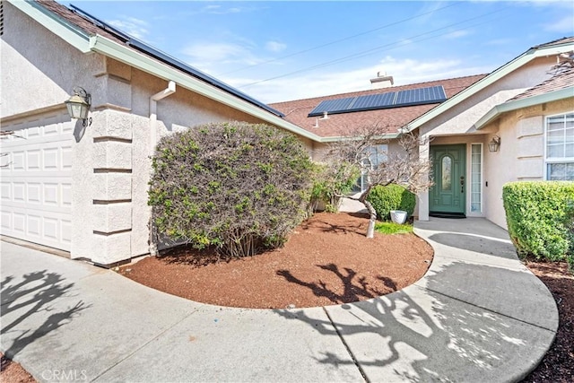 entrance to property featuring an attached garage, roof mounted solar panels, and stucco siding