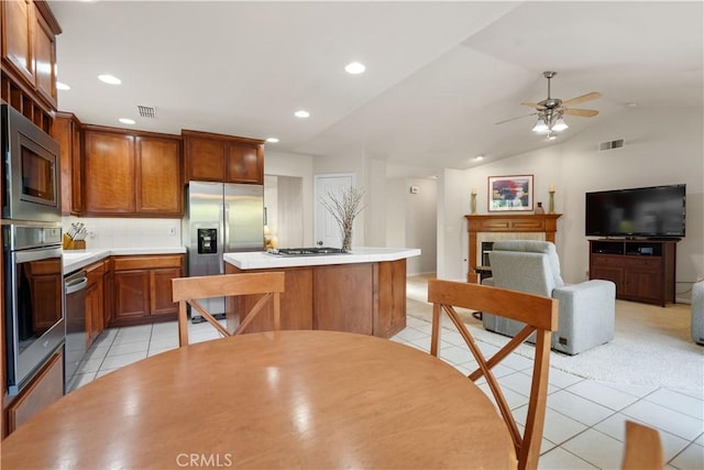 kitchen with light tile patterned floors, lofted ceiling, a kitchen island, light countertops, and appliances with stainless steel finishes