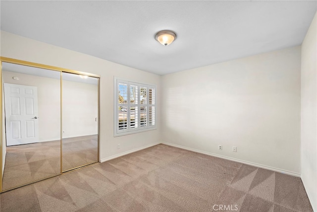 unfurnished bedroom featuring light carpet, a closet, and baseboards