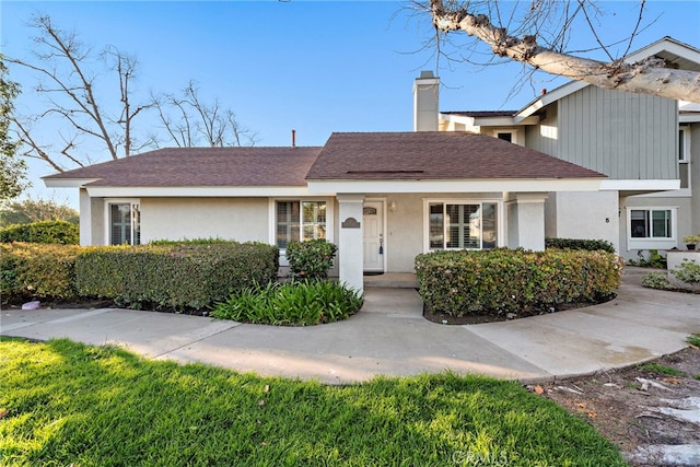 view of front of property with a shingled roof, a chimney, and stucco siding