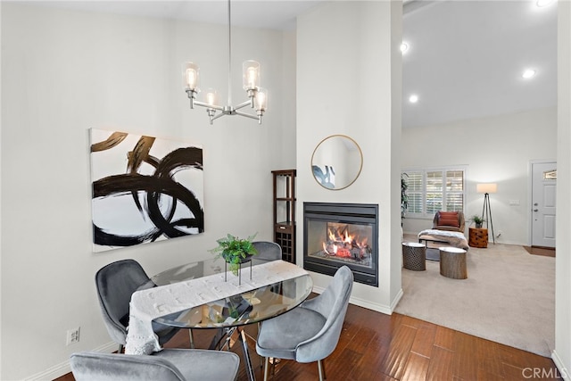 dining space featuring a chandelier, a high ceiling, baseboards, dark wood-style floors, and a glass covered fireplace