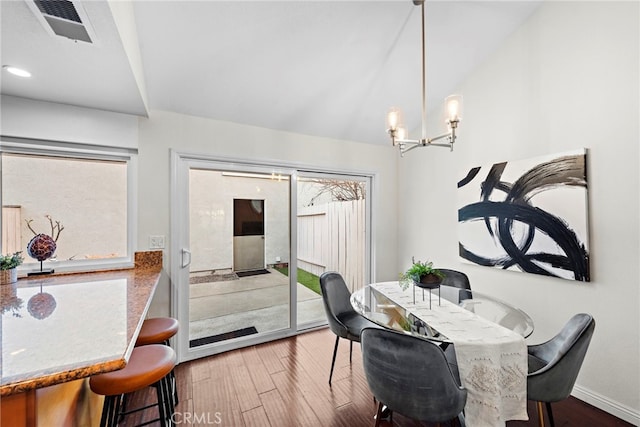 dining room with a chandelier, wood finished floors, visible vents, baseboards, and vaulted ceiling