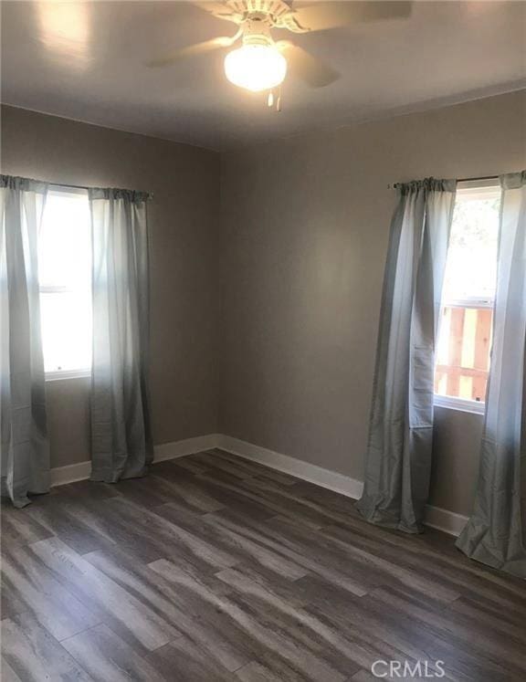 unfurnished room featuring dark wood-type flooring, a ceiling fan, a wealth of natural light, and baseboards