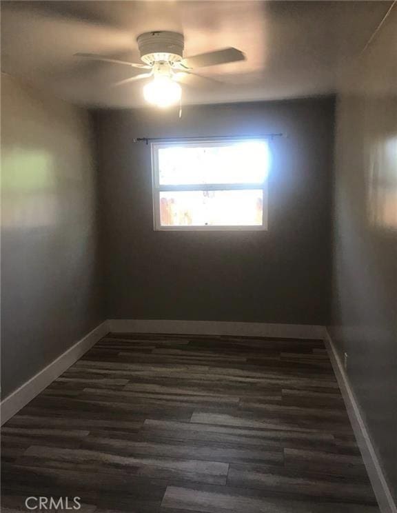 unfurnished room featuring dark wood finished floors, baseboards, and ceiling fan