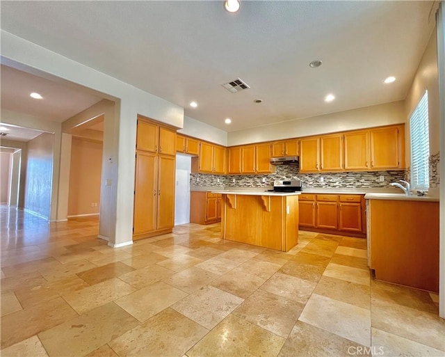 kitchen featuring visible vents, a kitchen breakfast bar, a center island, light countertops, and under cabinet range hood