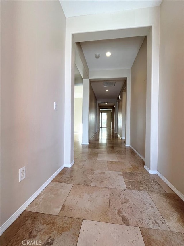 corridor featuring visible vents, baseboards, and stone tile flooring