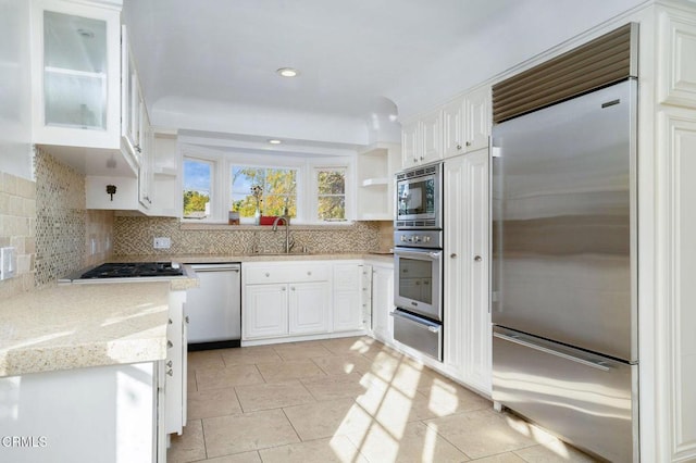 kitchen with white cabinets, glass insert cabinets, built in appliances, a sink, and a warming drawer