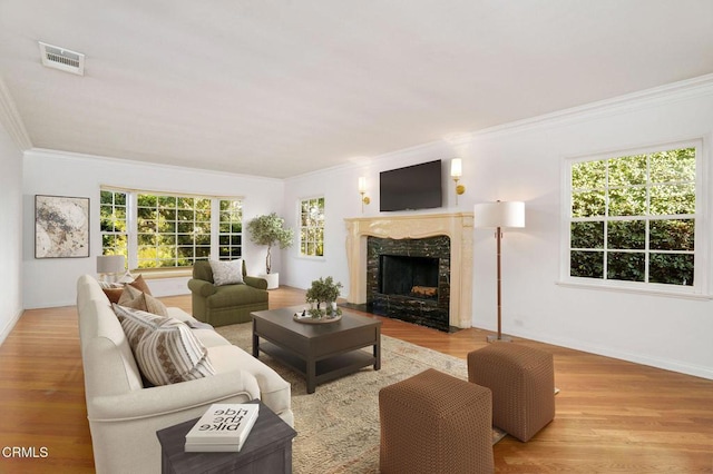 living room with a fireplace, visible vents, baseboards, light wood-style floors, and ornamental molding