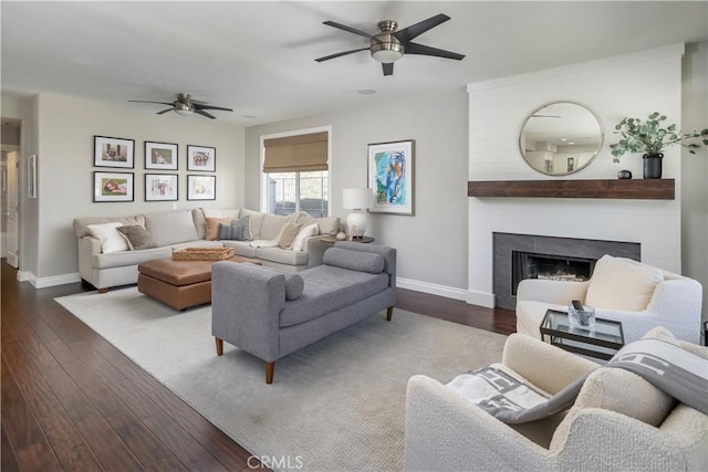 living area with a ceiling fan, a large fireplace, baseboards, and dark wood-style flooring