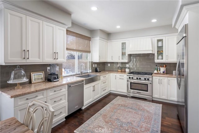 kitchen with stainless steel appliances, custom range hood, glass insert cabinets, white cabinetry, and a sink