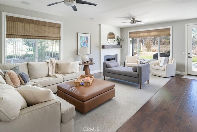 living area featuring dark wood-style floors, a fireplace, baseboards, and a ceiling fan