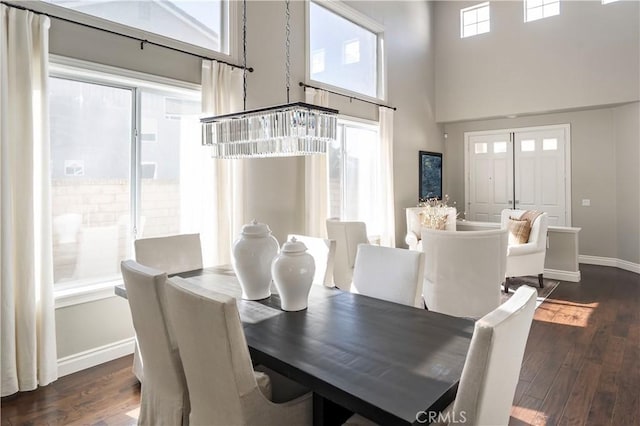 dining area featuring a chandelier, dark wood finished floors, a towering ceiling, and baseboards