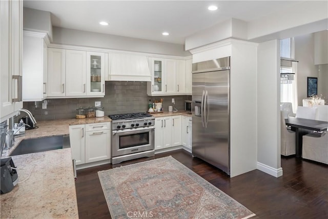 kitchen with premium appliances, a sink, white cabinetry, light stone countertops, and glass insert cabinets