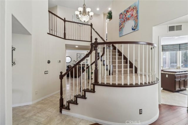 staircase featuring a notable chandelier, a high ceiling, wood finished floors, visible vents, and baseboards