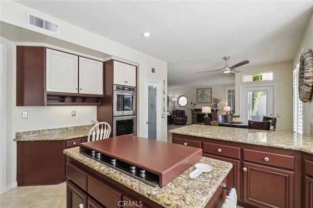 kitchen featuring stainless steel double oven, visible vents, a kitchen island, and light stone countertops