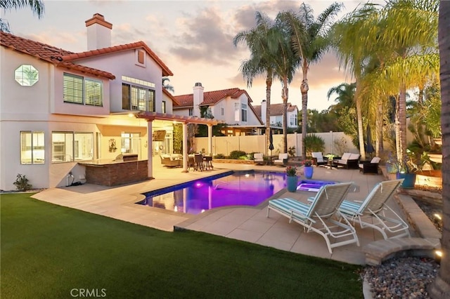 pool at dusk with a fenced in pool, fence, an outdoor kitchen, and a patio