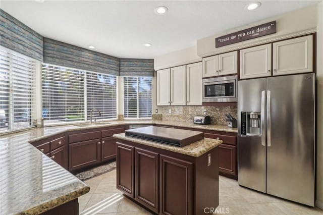 kitchen with light stone counters, stainless steel appliances, a kitchen island, a sink, and dark brown cabinets