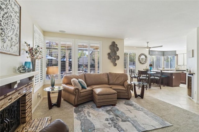 living room featuring wine cooler, light tile patterned floors, a ceiling fan, a glass covered fireplace, and light carpet