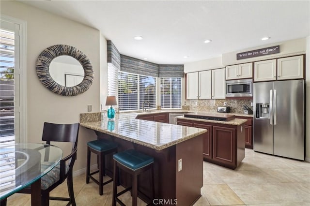 kitchen with stainless steel appliances, backsplash, a peninsula, and light stone counters