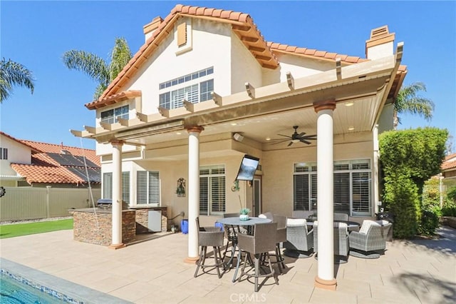 rear view of house featuring an outdoor kitchen, fence, a ceiling fan, a chimney, and a patio area