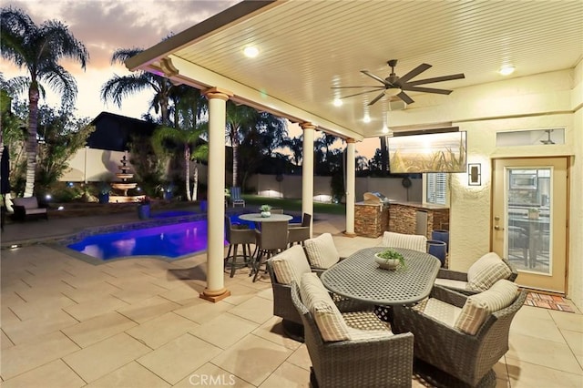 patio terrace at dusk featuring a ceiling fan, outdoor dining space, a fenced backyard, and area for grilling