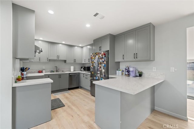 kitchen featuring visible vents, a peninsula, stainless steel appliances, light countertops, and a sink