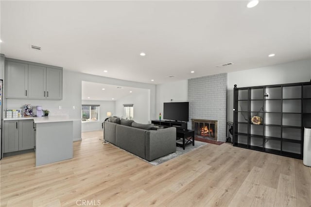 living room featuring light wood-type flooring, visible vents, and a fireplace