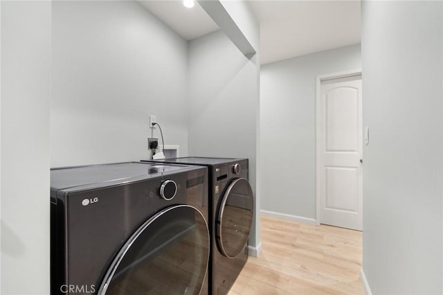 clothes washing area featuring light wood-type flooring, washing machine and clothes dryer, and baseboards