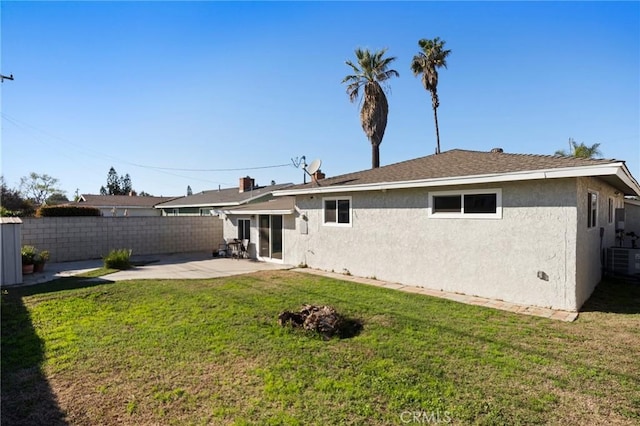 rear view of property featuring central AC unit, fence, a yard, stucco siding, and a patio area