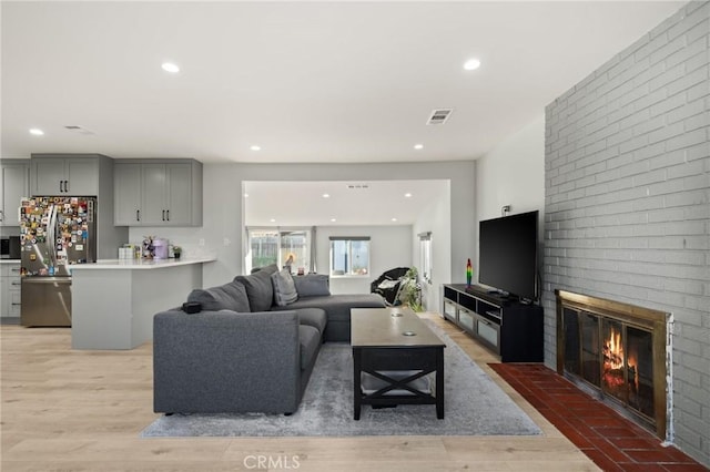 living room featuring a brick fireplace, visible vents, light wood finished floors, and recessed lighting