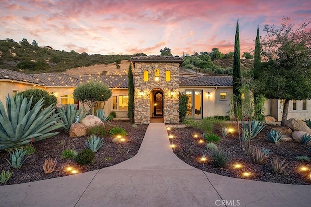 mediterranean / spanish-style house with stone siding, a tiled roof, and stucco siding