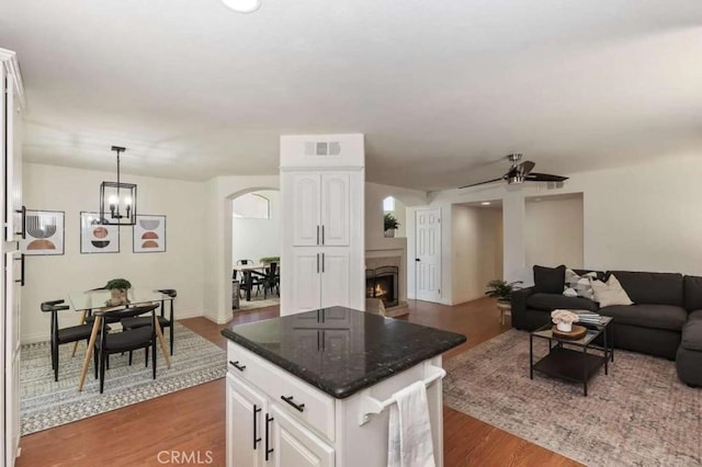 kitchen with arched walkways, a kitchen island, open floor plan, white cabinetry, and pendant lighting