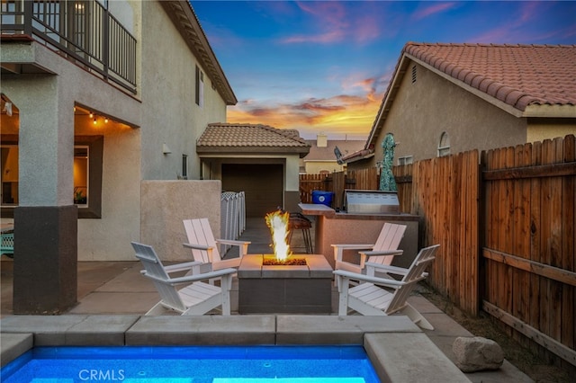 pool at dusk with fence private yard, a patio area, a fire pit, and exterior kitchen