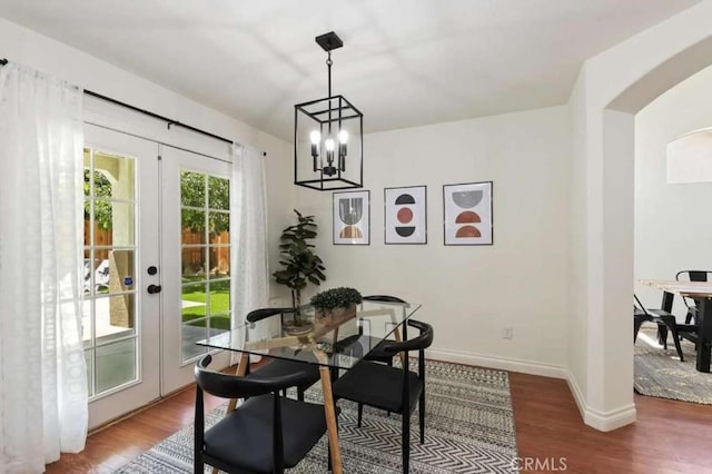 dining room with a notable chandelier, baseboards, arched walkways, and wood finished floors